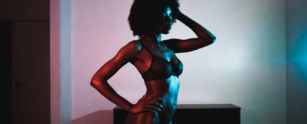 Stylish ebony woman posing in lingerie with neon lighting